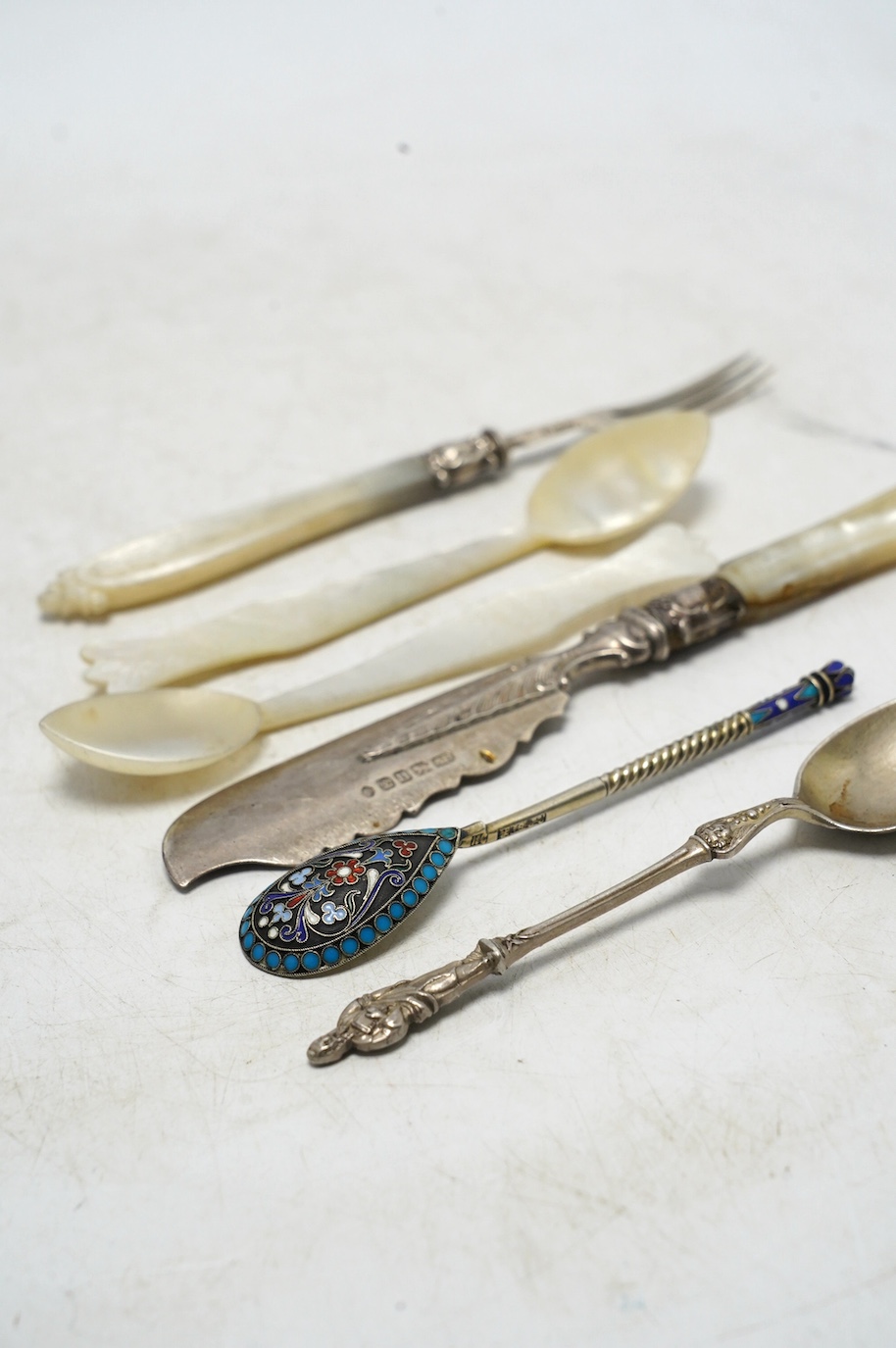 A small group of assorted silver and white metal cutlery including teaspoons, mother of pearl handled butter knives, a set of eight modern silver fiddle and shell pattern handled table knives and a matching set of eight